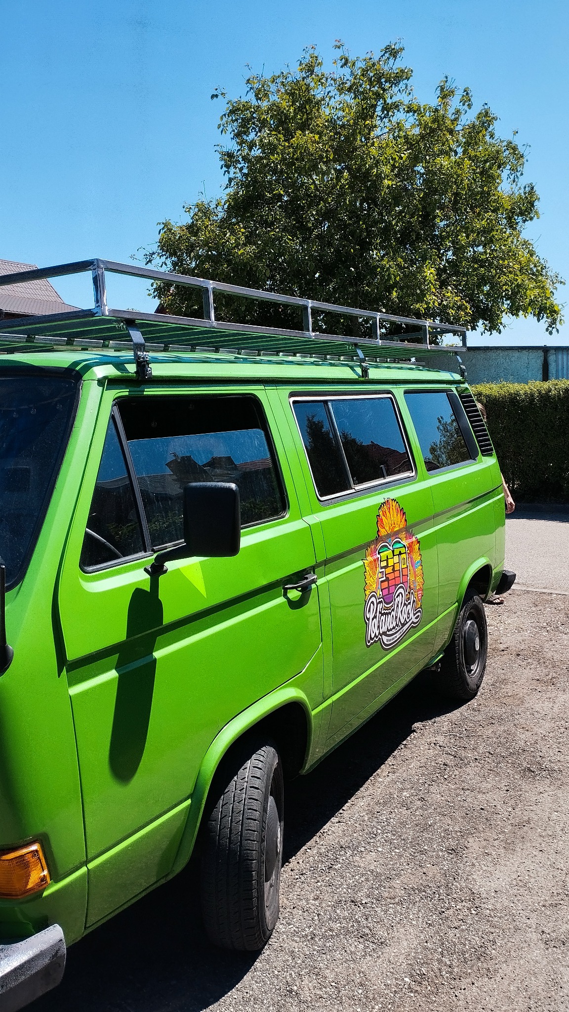 Zielony bus VW z metalowym bagażnikiem dachowym na tle drzewa i nieba. Bagażnik wykonany ze spawanych, metalowych rurek.