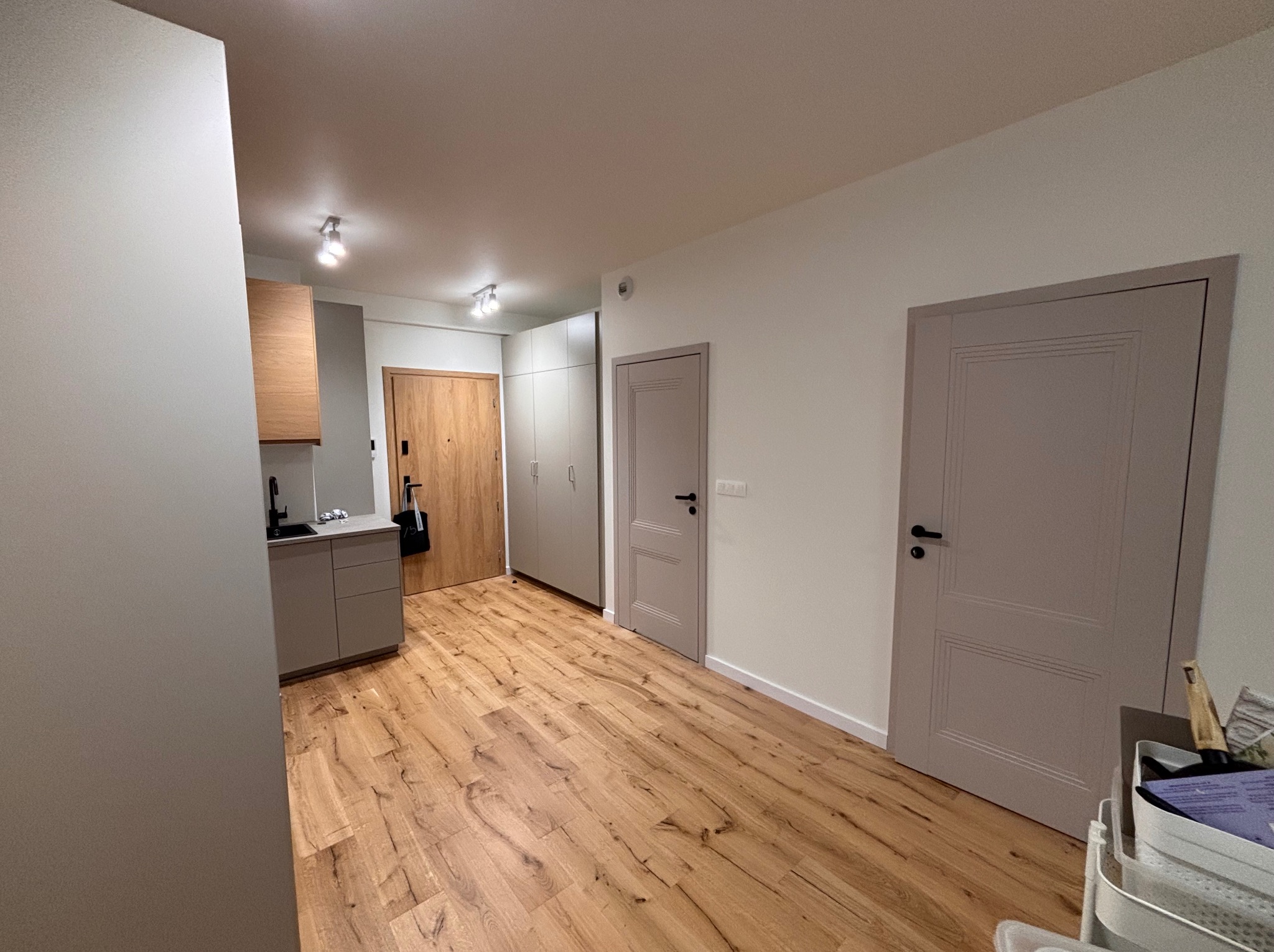 Jasne panele podłogowe i szare drzwi po remoncie w Będzinie. Widok na odnowione wnętrze mieszkania z elementami zabudowy kuchennej i szaf.