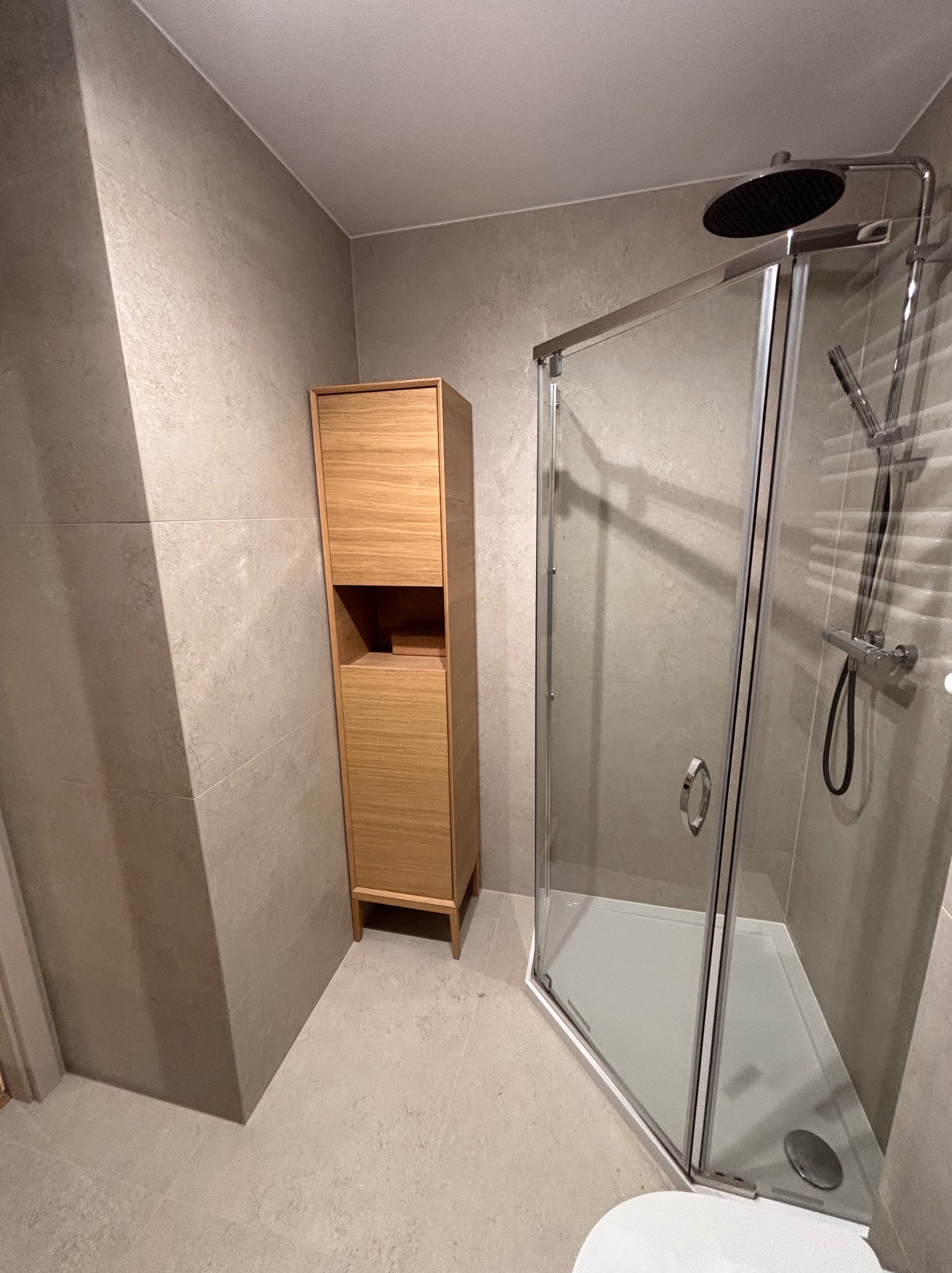 Nowoczesna łazienka z kabiną prysznicową i drewnianą szafką. Stonowana kolorystyka, płytki imitujące kamień. Minimalistyczny design.