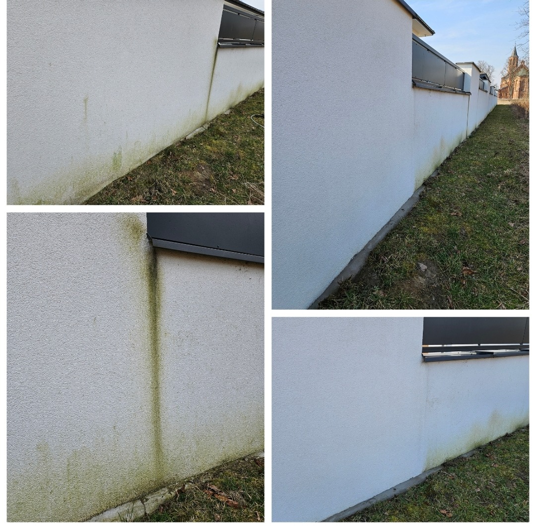 Fragment elewacji budynku z widocznymi zabrudzeniami i śladami porostu glonów, zarys dachu i fragment trawnika w tle.