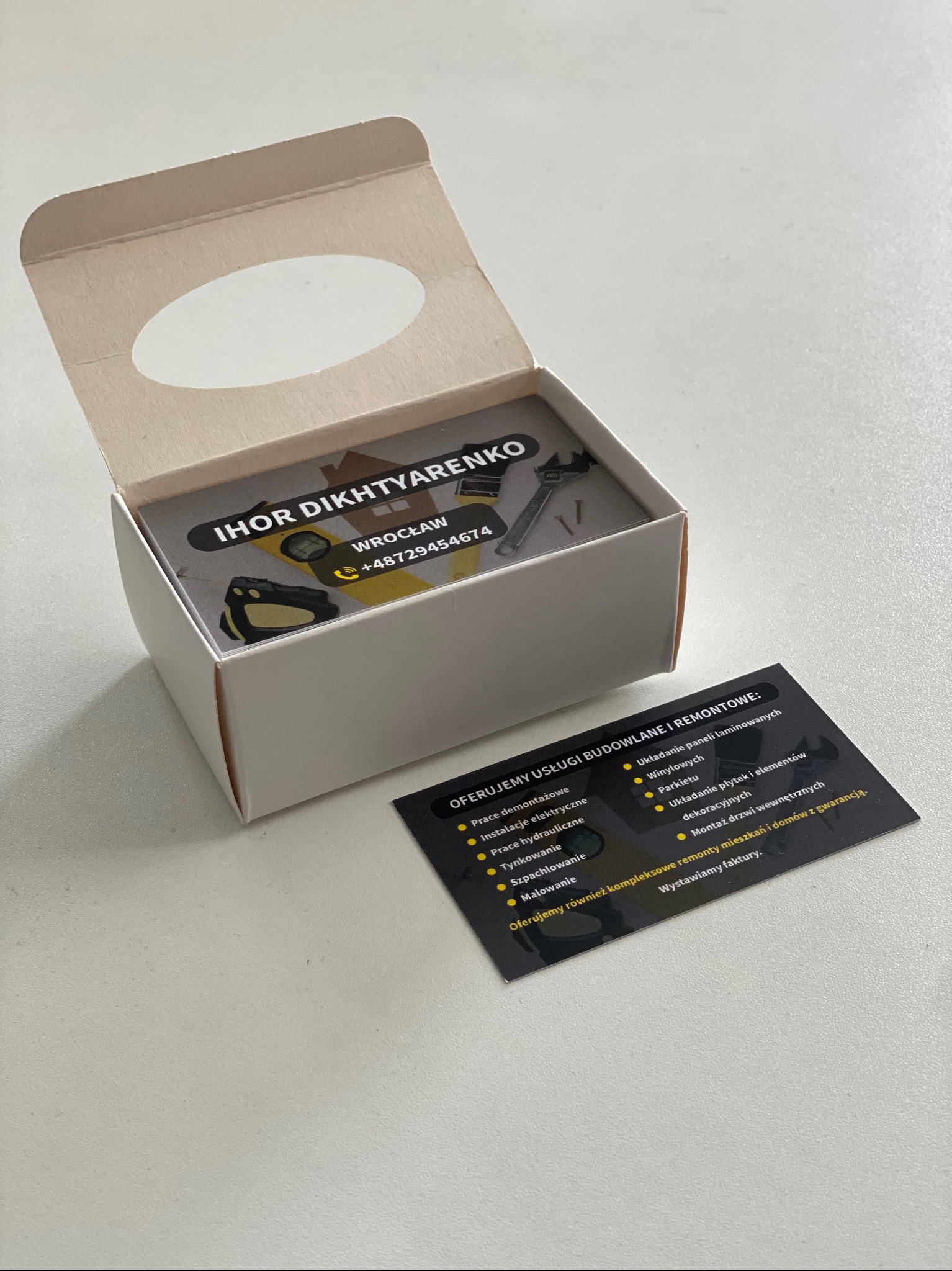 Pudełko wizytówek z danymi kontaktowymi firmy remontowo-budowlanej IHOR DIKHTYARENKO, wraz z dodatkową wizytówką z ofertą usług, na jasnym tle.