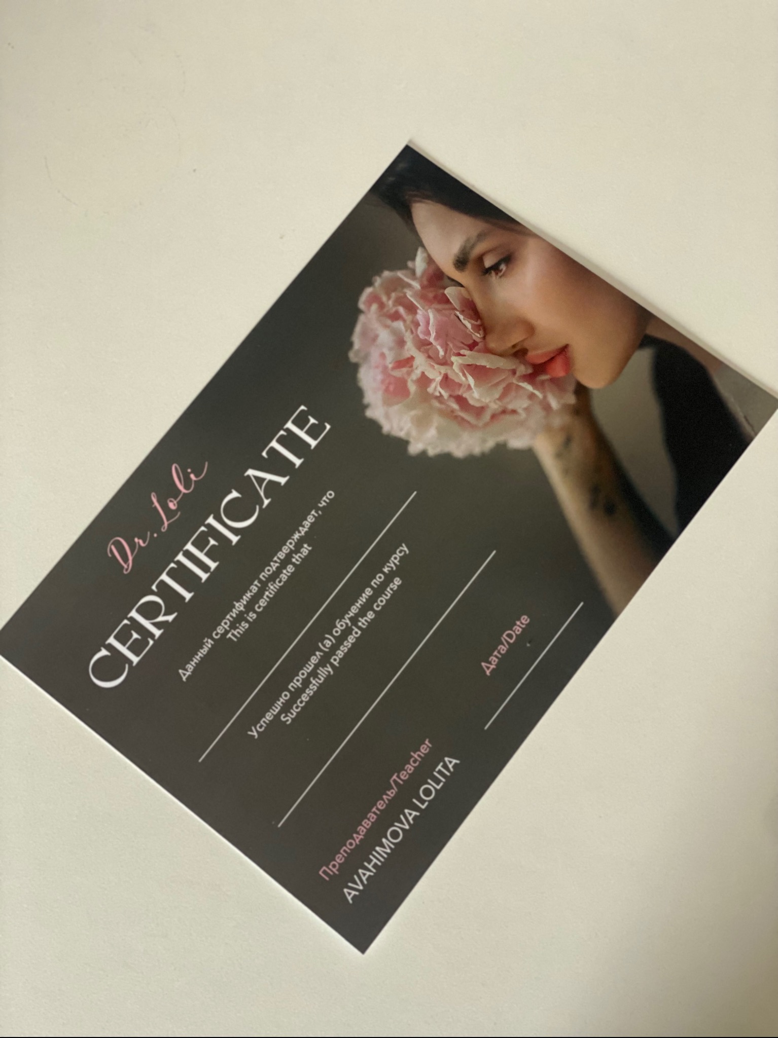 Czarno-różowy certyfikat z wizerunkiem kobiety i kwiatów, leżący ukośnie na jasnym tle. Dokument w języku rosyjskim i angielskim, z napisem 'Dr. Loli CERTIFICATE'.