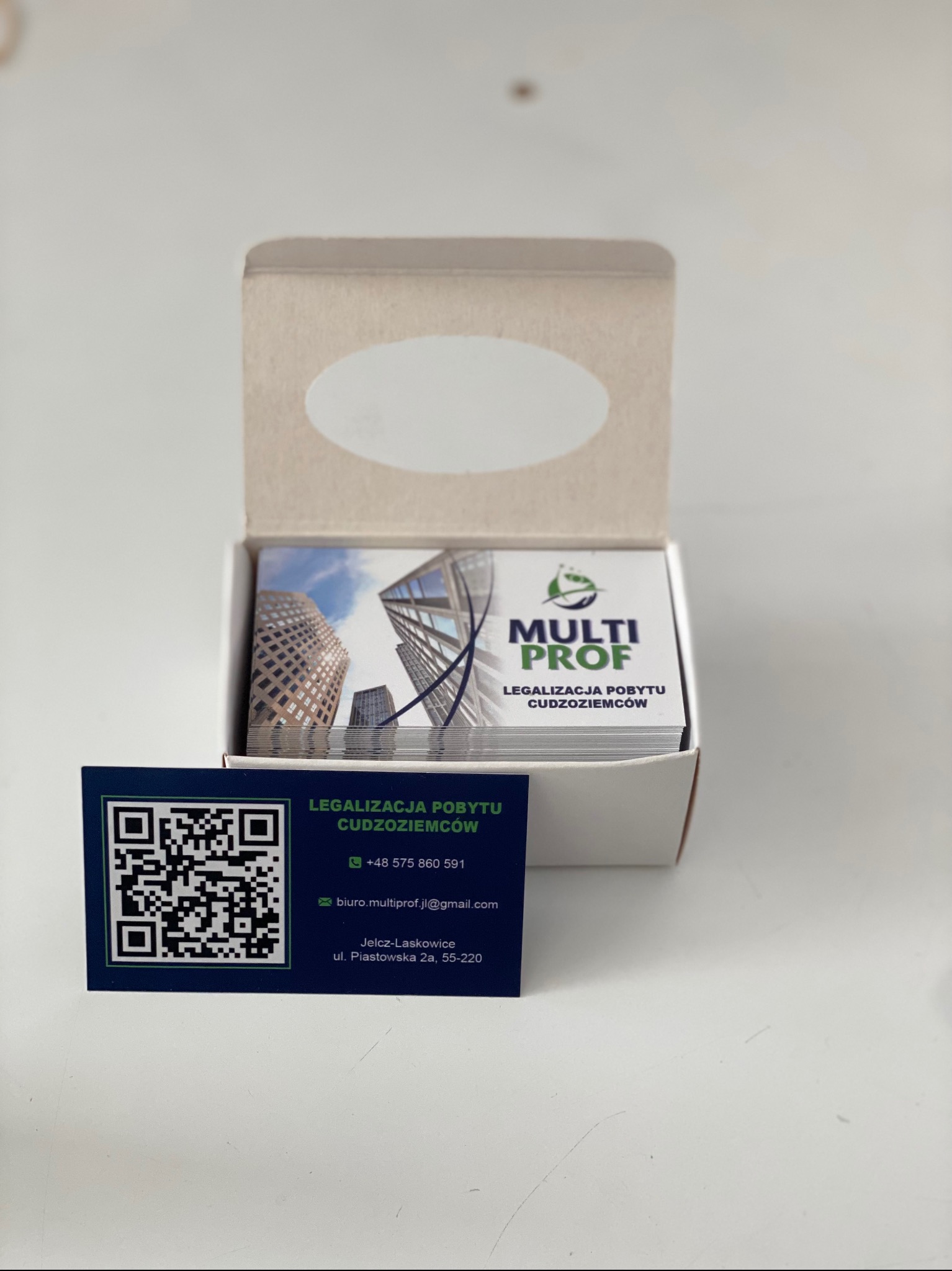 Pudełko z wizytówkami firmy Multi Prof, specjalizującej się w legalizacji pobytu cudzoziemców. Na pierwszej wizytówce widoczny kod QR.