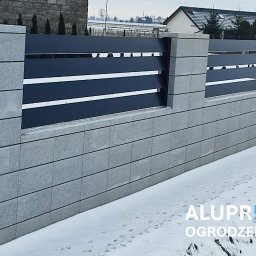 ALUPREM ZBIGNIEW OLCZAK - Nowoczesne ogrodzenie z szarej, betonowej podmurówki i czarnych, poziomych paneli, widok z zewnątrz w zimowej scenerii.