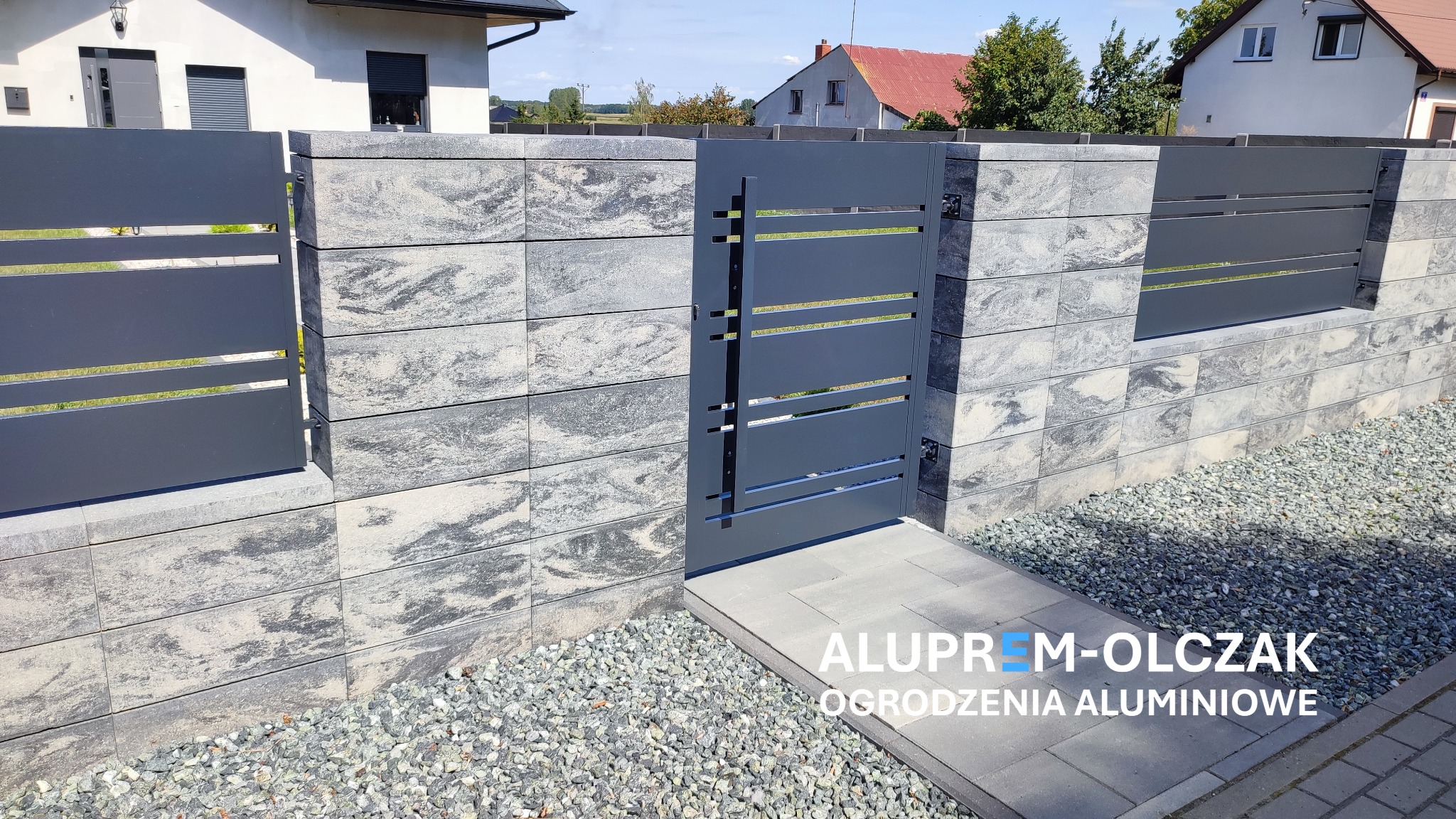 Nowoczesna brama wejściowa z poziomymi szczeblami w szarym kolorze, wkomponowana w ogrodzenie z bloczków imitujących kamień, z widocznymi elementami mocującymi i ścieżką z szarych płyt prowadzącą...