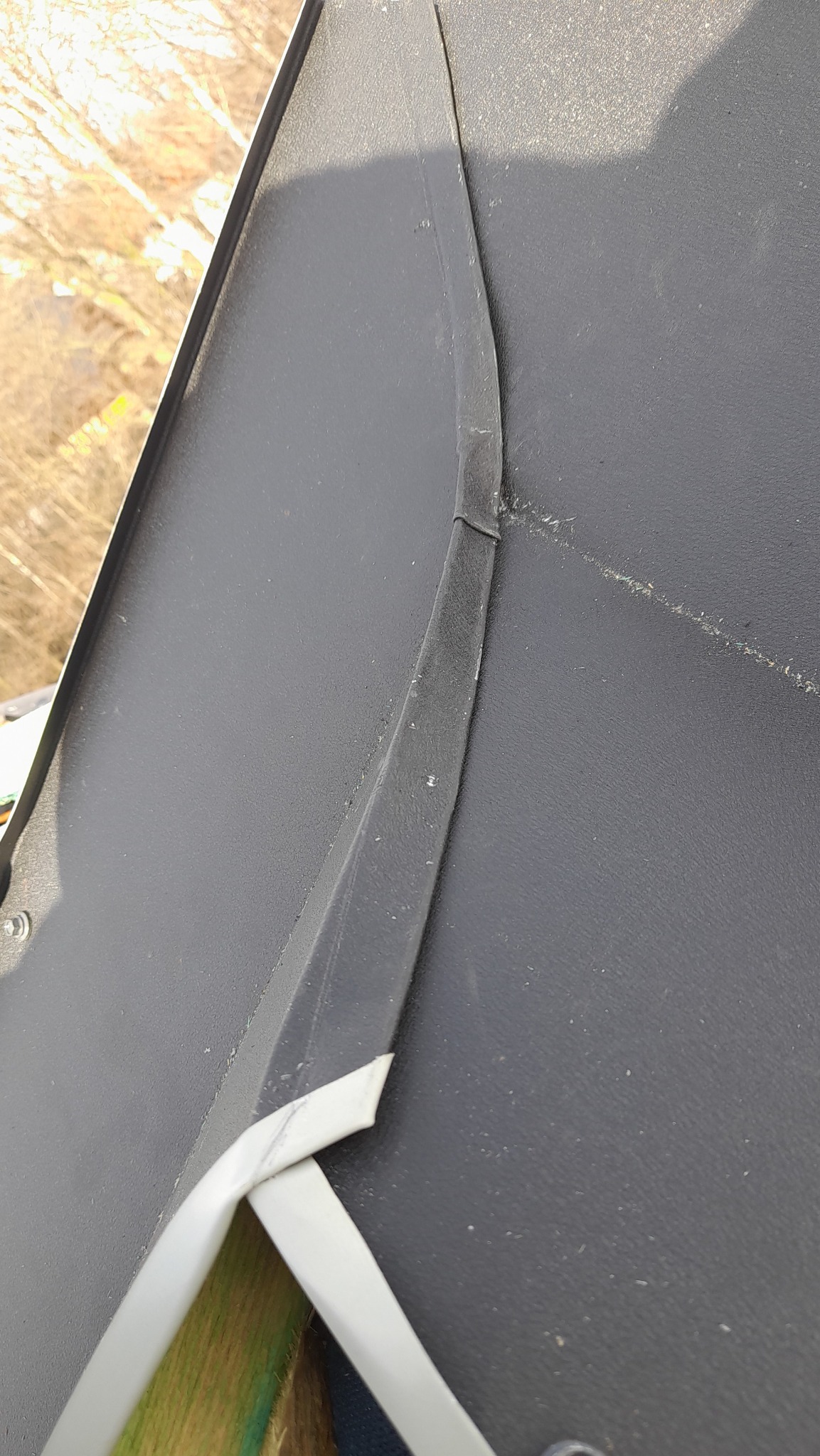 Szczegółowe ujęcie fragmentu dachu z widocznymi obróbkami blacharskimi, ukazujące łączenie blachy i elementy mocujące, z drzewami w tle.