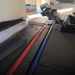 HYDRATOM TOMASZ ŻYHALUK - Czerwona i niebieska rura instalacji grzewczej ułożona w bruzdach w podłodze, obok rozłożona skrzynka z narzędziami.