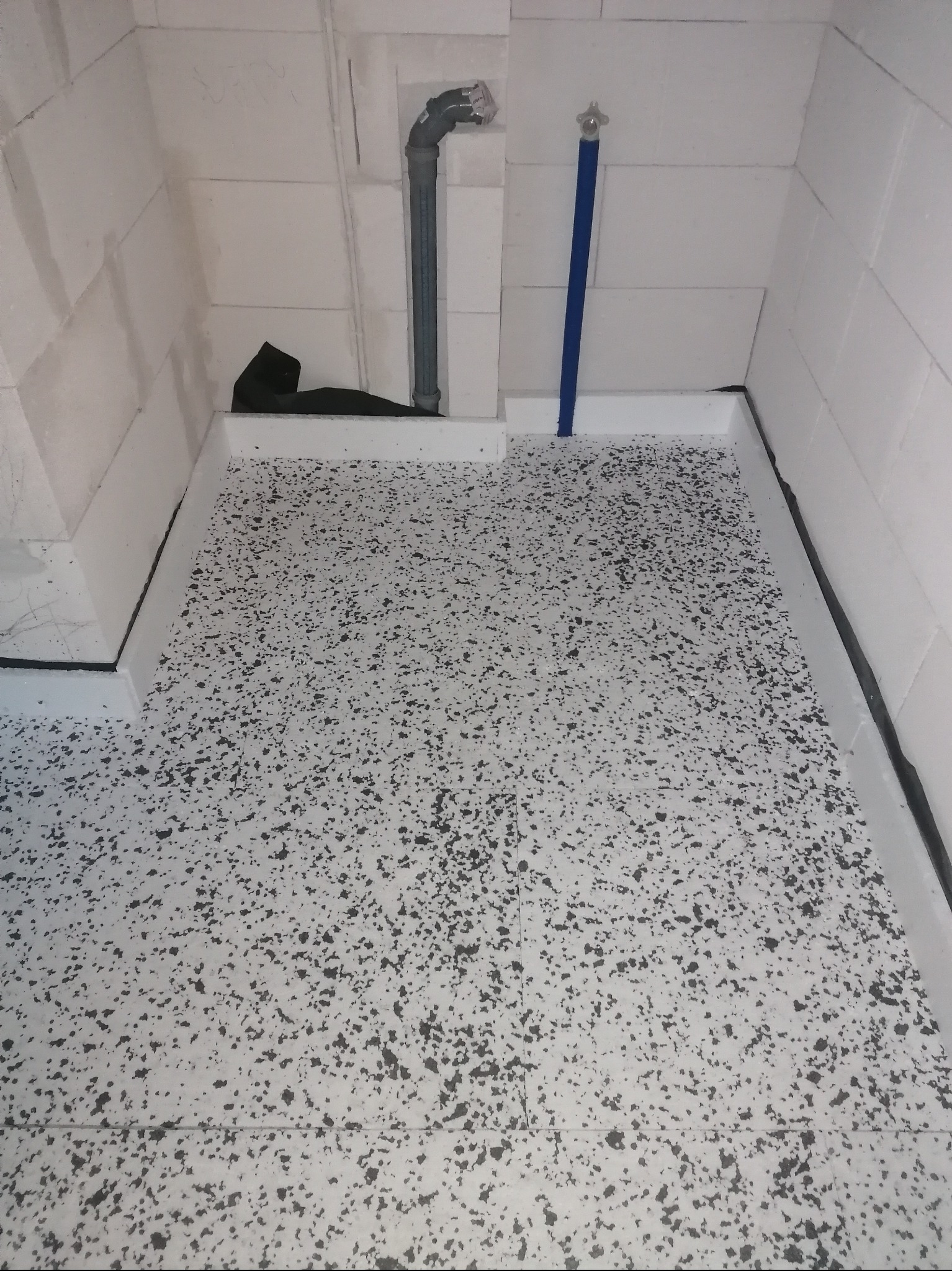 Przygotowane podłoże z hydroizolacją i odpływem liniowym w narożniku pomieszczenia z bloczków betonowych, gotowe do ułożenia płytek w kabinie prysznicowej.