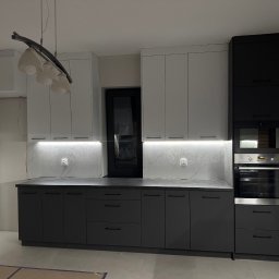 WYMIAROWE STUDIO MEBLI MICHAŁ ZALEWSKI - Nowoczesna kuchnia z białymi górnymi szafkami i grafitowymi dolnymi, oświetlenie LED pod szafkami, czarne okno w tle, lampa wisząca z kilkoma białymi kloszami.