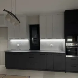 Nowoczesna kuchnia z białymi g&oacute;rnymi szafkami i grafitowymi dolnymi, oświetlenie LED pod szafkami, czarne okno w tle, lampa wisząca z kilkoma białymi kloszami.