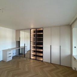 WYMIAROWE STUDIO MEBLI MICHAŁ ZALEWSKI - Jasna szafa wnękowa z biurkiem i podświetlaną witryną, parkiet w jodełkę. Minimalistyczny design, czarne uchwyty. Nowoczesne meble na wymiar.