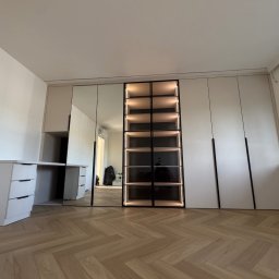 WYMIAROWE STUDIO MEBLI MICHAŁ ZALEWSKI - Nowoczesna szafa wnękowa z lustrami i oświetleniem LED, połączona z biurkiem, na parkiecie ułożonym w jodełkę, w jasnym wnętrzu.