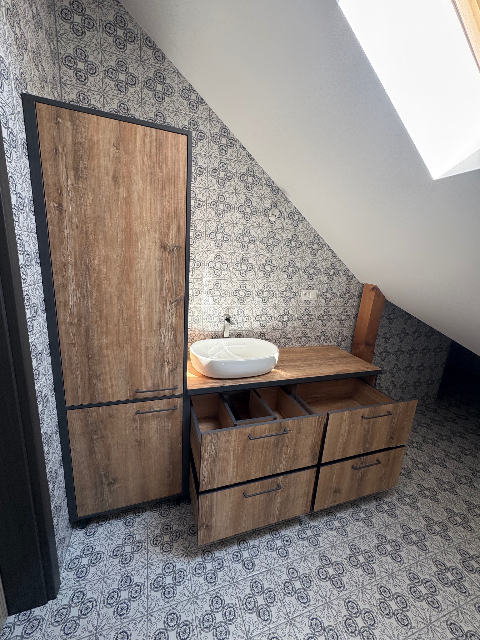 Łazienka na poddaszu z drewnianą szafką z szufladami, umywalką nablatową i wzorzystymi płytkami na ścianach i podłodze, w stylu nowoczesnym.