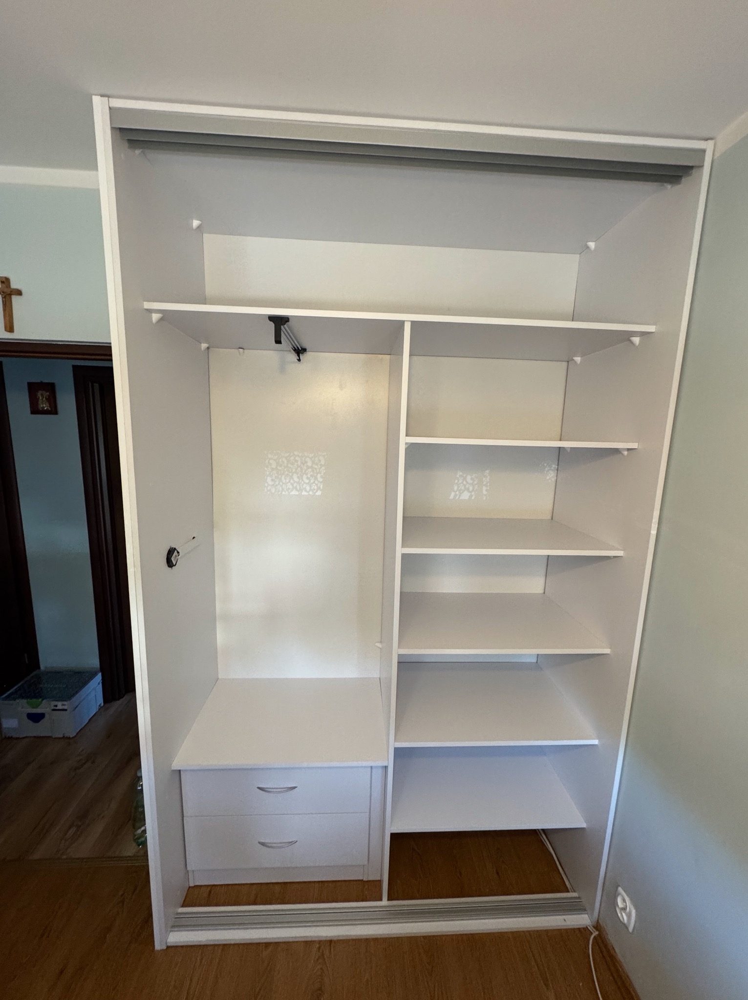 Biała, otwarta szafa wnękowa z półkami i szufladami, widok z przodu. Realizacja z Ośna Drugiego. Minimalistyczny design, jasne wnętrze.