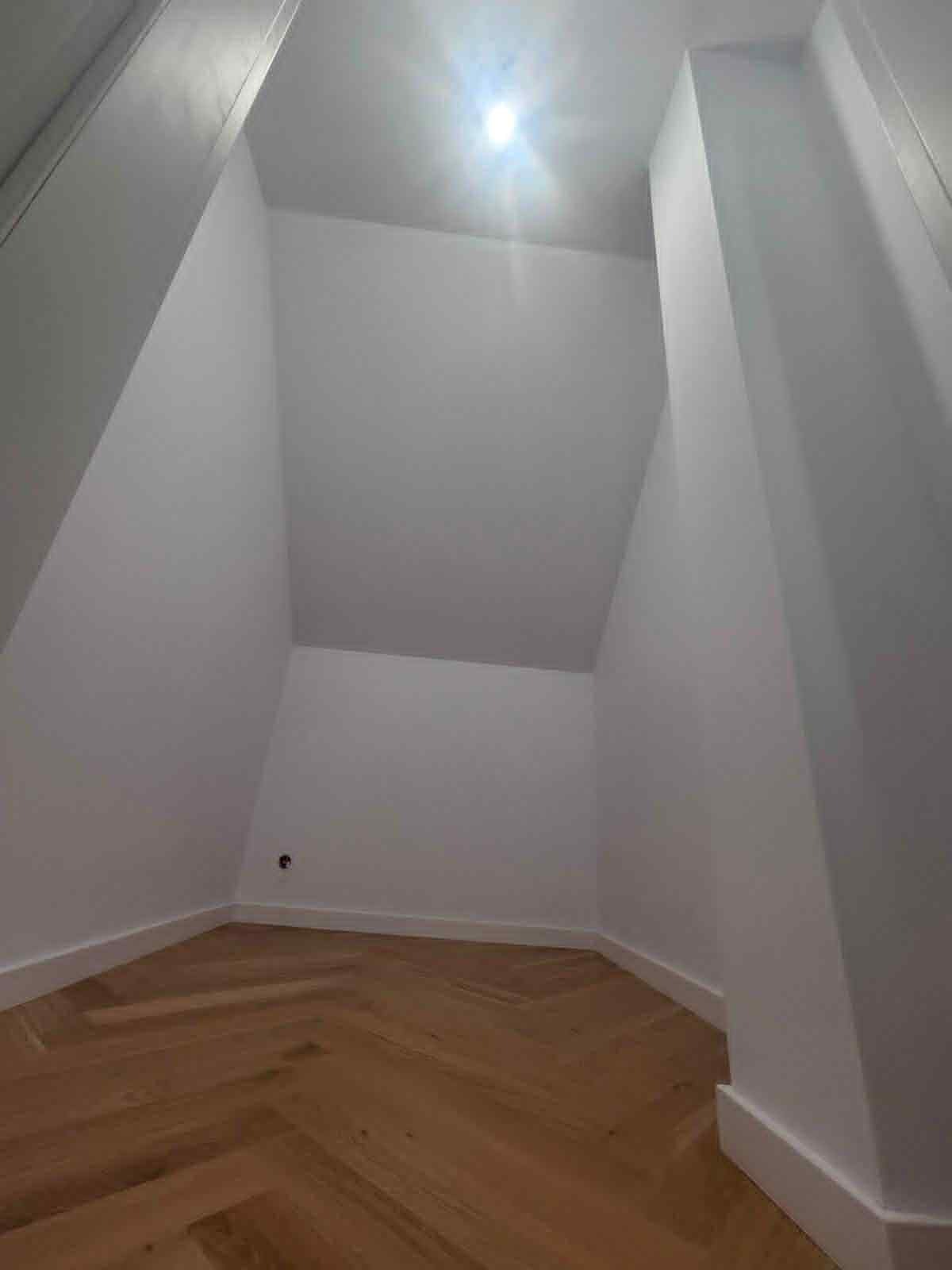 Wnętrze po remoncie: białe ściany i parkiet ułożony w jodełkę, listwy przypodłogowe. Widok na poddasze ze skosami i punktowym oświetleniem.