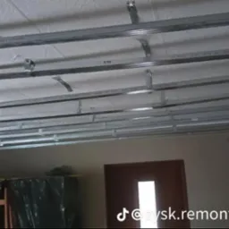 Montaż metalowej konstrukcji sufitu podwieszanego z płyt kartonowo-gipsowych, widoczny szkielet z profili na tle białego sufitu i fragmentu ściany.