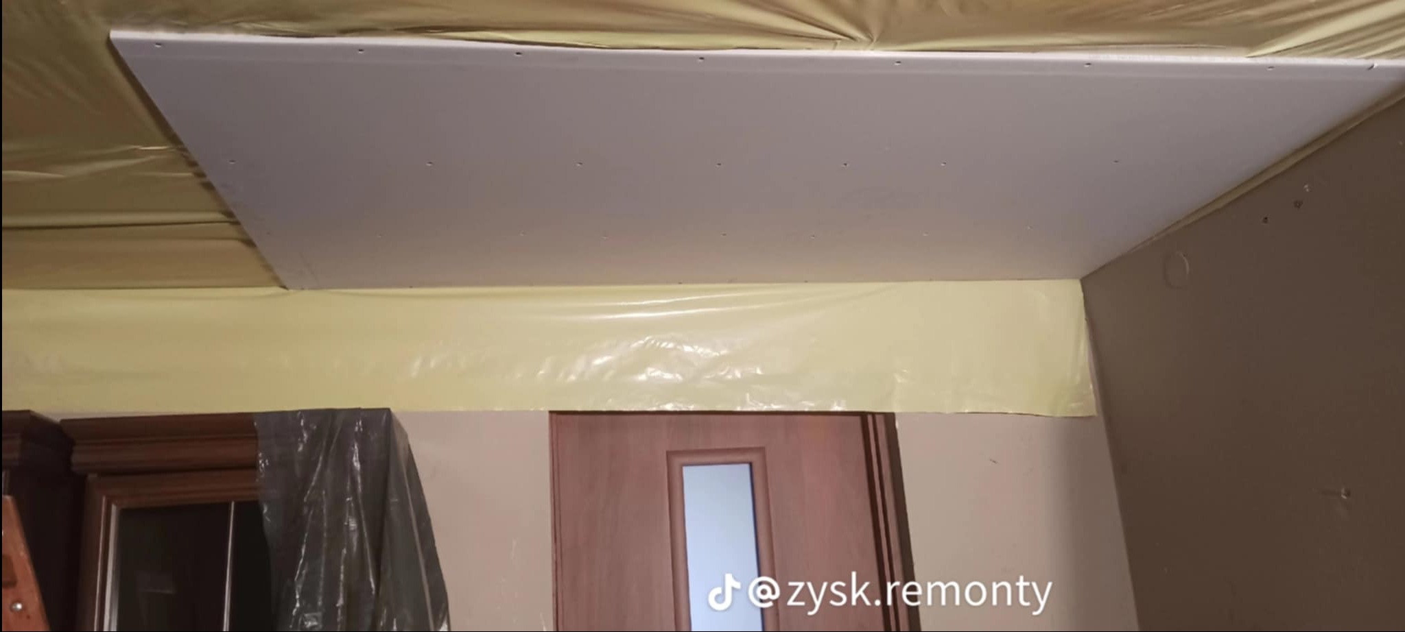 Montaż płyty gipsowo-kartonowej na suficie, folia ochronna zabezpiecza ściany i meble podczas prac.