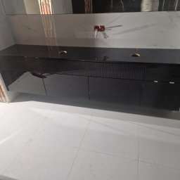 Łukasz Stolarz - Czarna, lakierowana szafka pod umywalkę z frezowanymi frontami, zamontowana w łazience w trakcie remontu, widoczne niedokończone ściany i instalacja elektryczna.