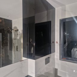 Łukasz Stolarz - Nowoczesna łazienka z czarnymi, lustrzanymi szafkami narożnymi, białymi marmurowymi płytkami ściennymi i czarną armaturą, w tym toaletą i oknem.