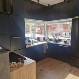 Łukasz Stolarz - Nowoczesna, czarna kuchnia z drewnianymi blatami w Aleksandrowie Łódzkim, widok na budowę przez duże okno, minimalistyczny design.
