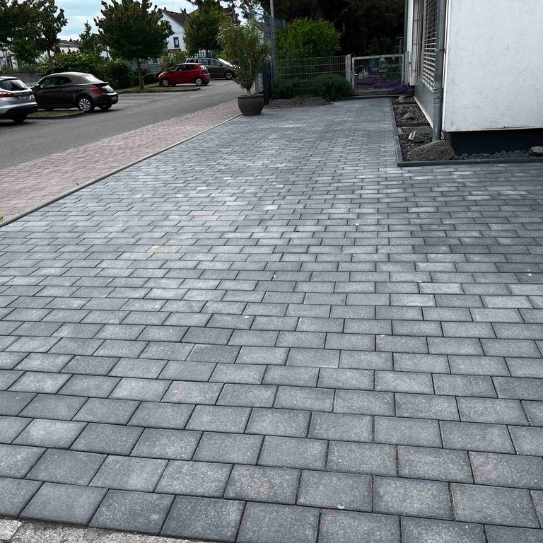 Ułożona szara kostka brukowa na podjeździe przed domem, widok z niskiej perspektywy, z donicą z rośliną przy krawędzi.