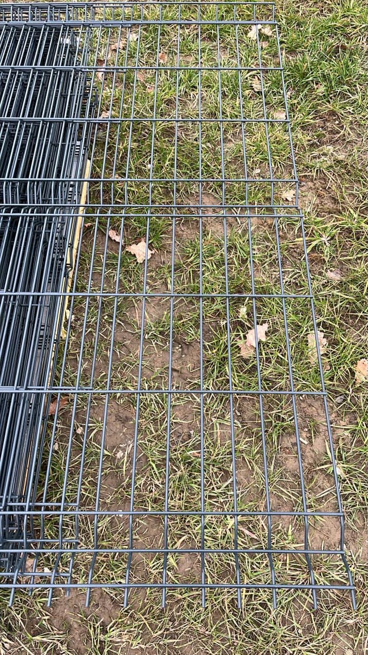 Stos paneli ogrodzeniowych zgrzewanych, leżących na trawie z widocznymi suchymi liśćmi, przygotowanych do transportu lub montażu.