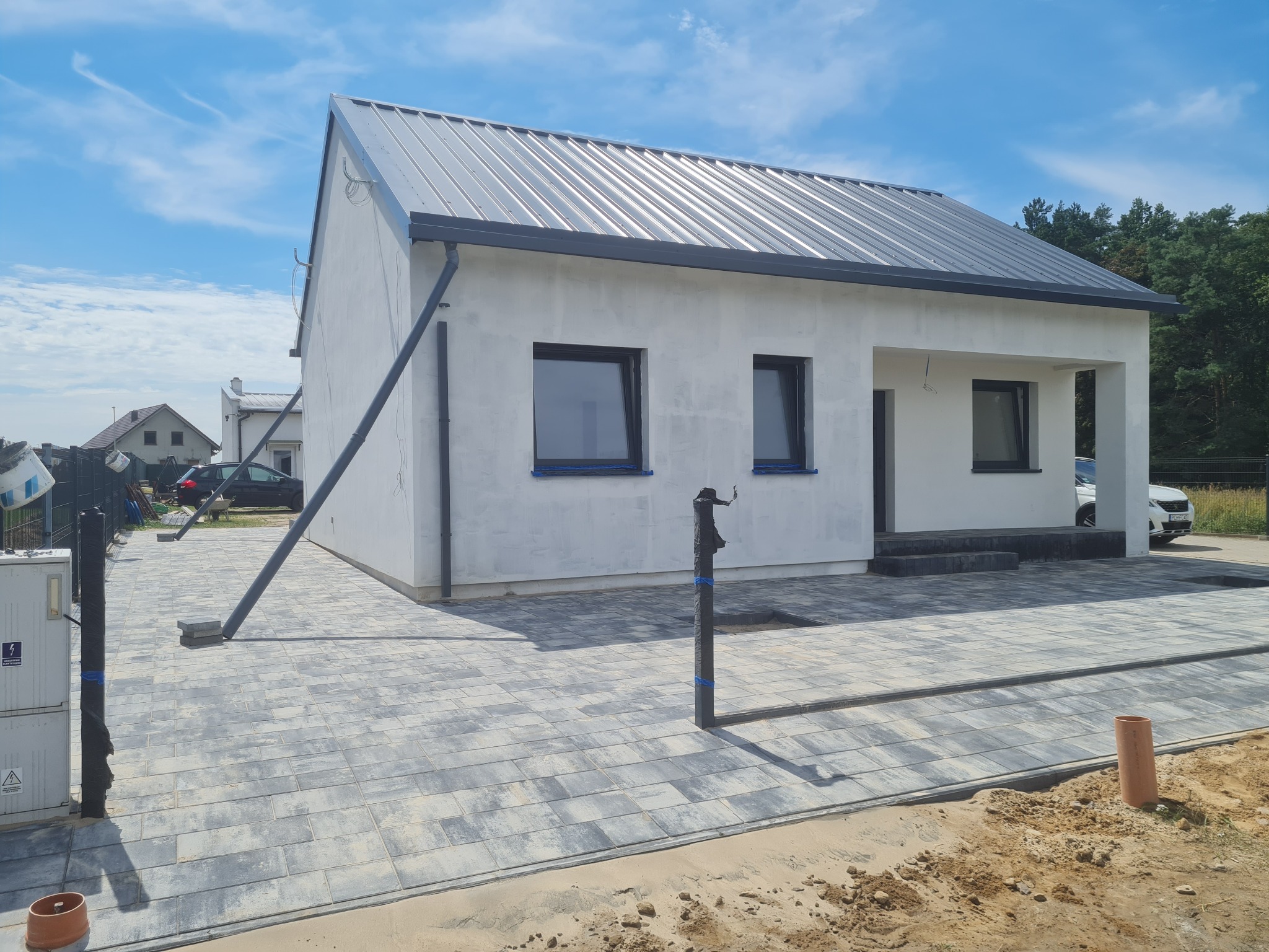 Nowoczesny dom jednorodzinny z szarą kostką brukową na podjeździe, widok z zewnątrz w słoneczny dzień. Kostka ułożona w regularny wzór, widoczne detale wykończenia.