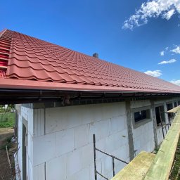 Styl Dach Mariia Popovych - Nowy dach z czerwonej blachodachówki, widok z rusztowania na budynek w trakcie budowy we Wrocławiu, rynna w kolorze grafitowym.