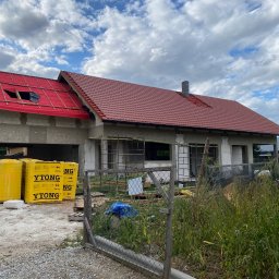 Styl Dach Mariia Popovych - Budowa domu w trakcie krycia dachu czerwoną dachówką, widoczne materiały budowlane YTONG i membrana dachowa, częściowo odkryta więźba dachowa.