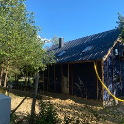 Styl Dach Mariia Popovych - Nowoczesny dom w trakcie budowy, z czarnym, metalowym pokryciem i oknami dachowymi, widoczna konstrukcja ścian i żółty przewód doprowadzony do budynku.