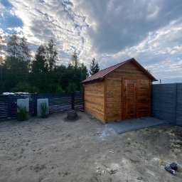 Styl Dach Mariia Popovych - Nowo postawiony, drewniany budynek gospodarczy z czerwoną blachą na dachu, widoczny na tle pochmurnego nieba i ogrodzenia.