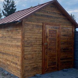 Styl Dach Mariia Popovych - Drewniany domek narzędziowy z brązowym metalowym wykończeniem dachu i rynnami, widok z przodu, na tle częściowo zachmurzonego nieba i ogrodzenia.