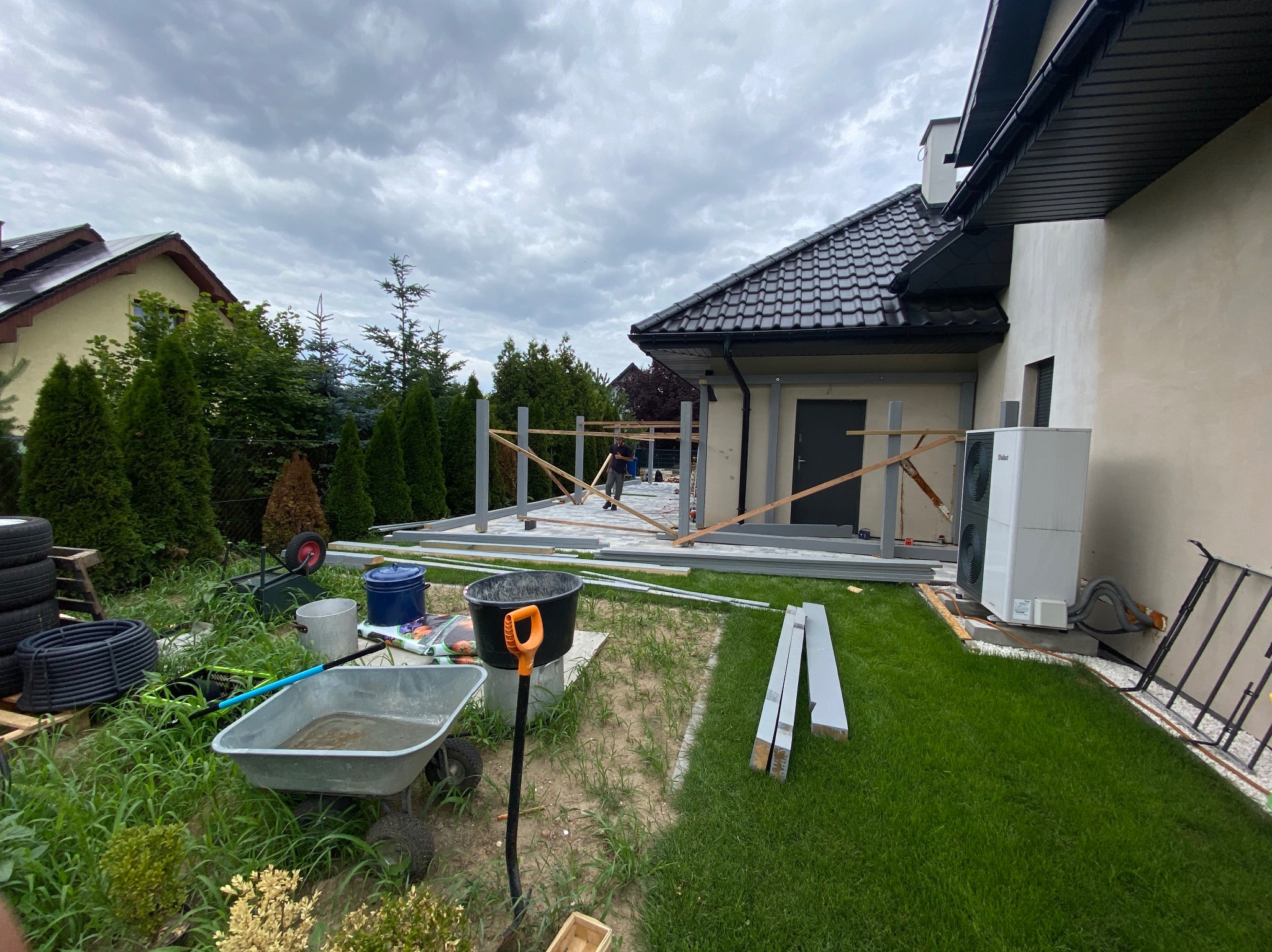 Montaż drewnianej konstrukcji zadaszenia tarasu przy domu we Wrocławiu, widoczne narzędzia i materiały budowlane, pochmurne niebo w tle.