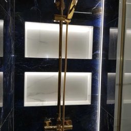 HOMES Adam Abramowicz - Nowoczesna kabina prysznicowa z armaturą w kolorze złotym, podświetlane wnęki w czarnych marmurowych płytkach.