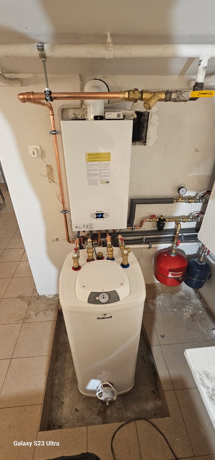 Biały piec gazowy z zasobnikiem Galmet, miedziane rury, zawory, manometr. Instalacja w piwnicy, widoczne elementy instalacji CO i CWU.