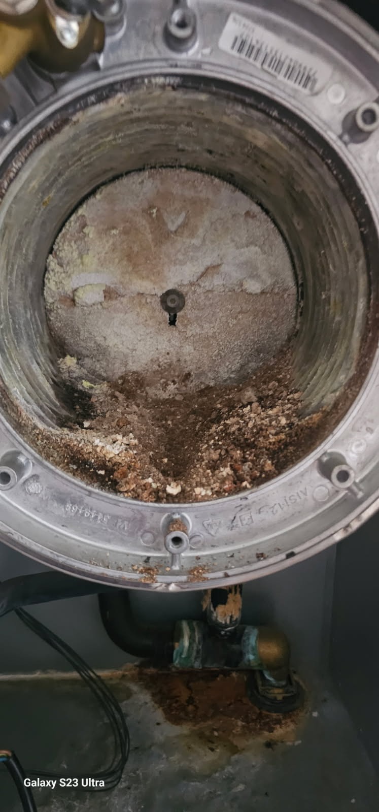 Wnętrze zardzewiałego pieca gazowego z osadami i korozją, widoczne rury i złącza z śladami wycieków. Niefachowe ujęcie z bliska.