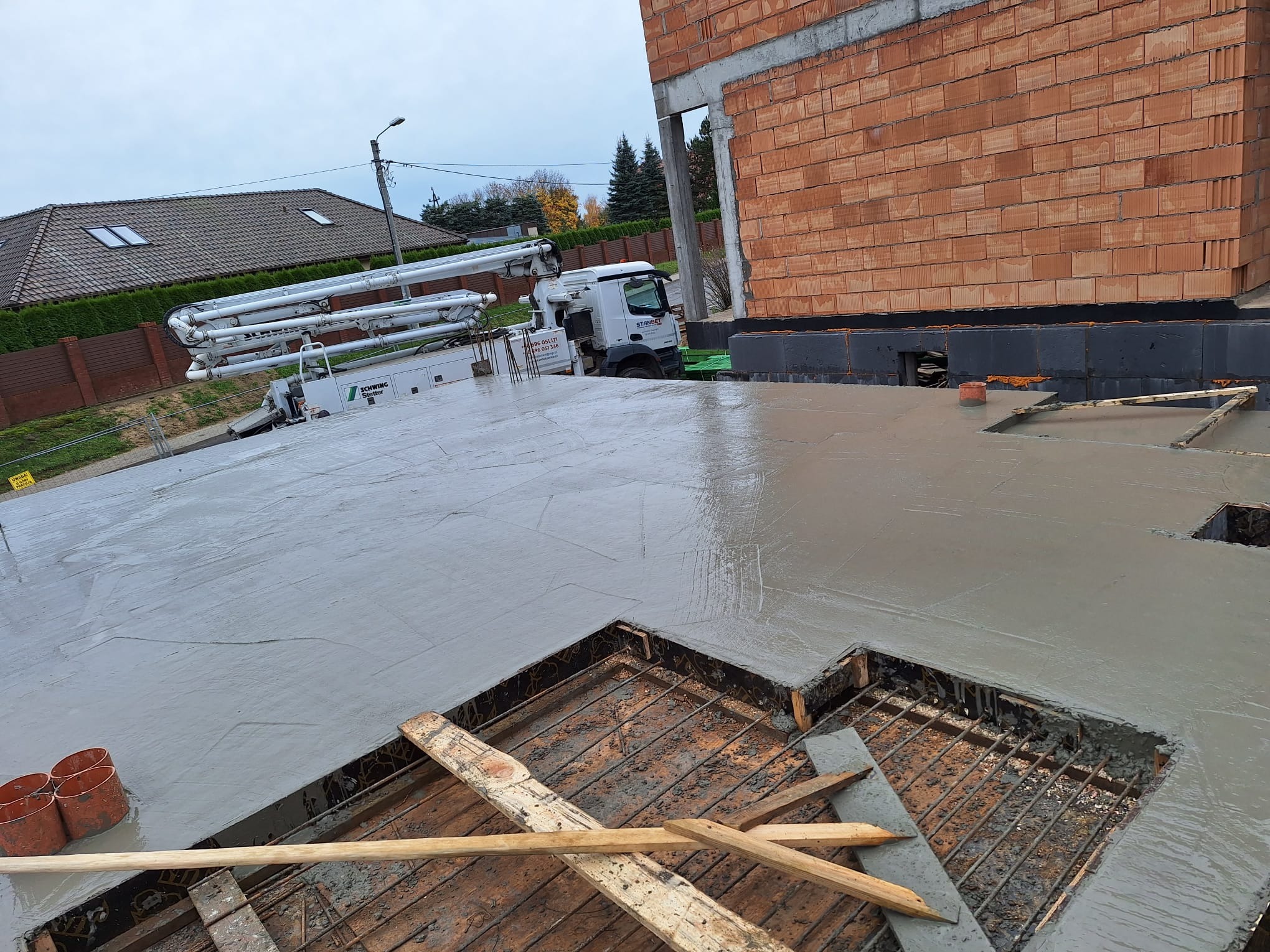 Wylewka betonowa na stropie domu jednorodzinnego, widoczna konstrukcja zbrojeniowa, pompa do betonu w tle.