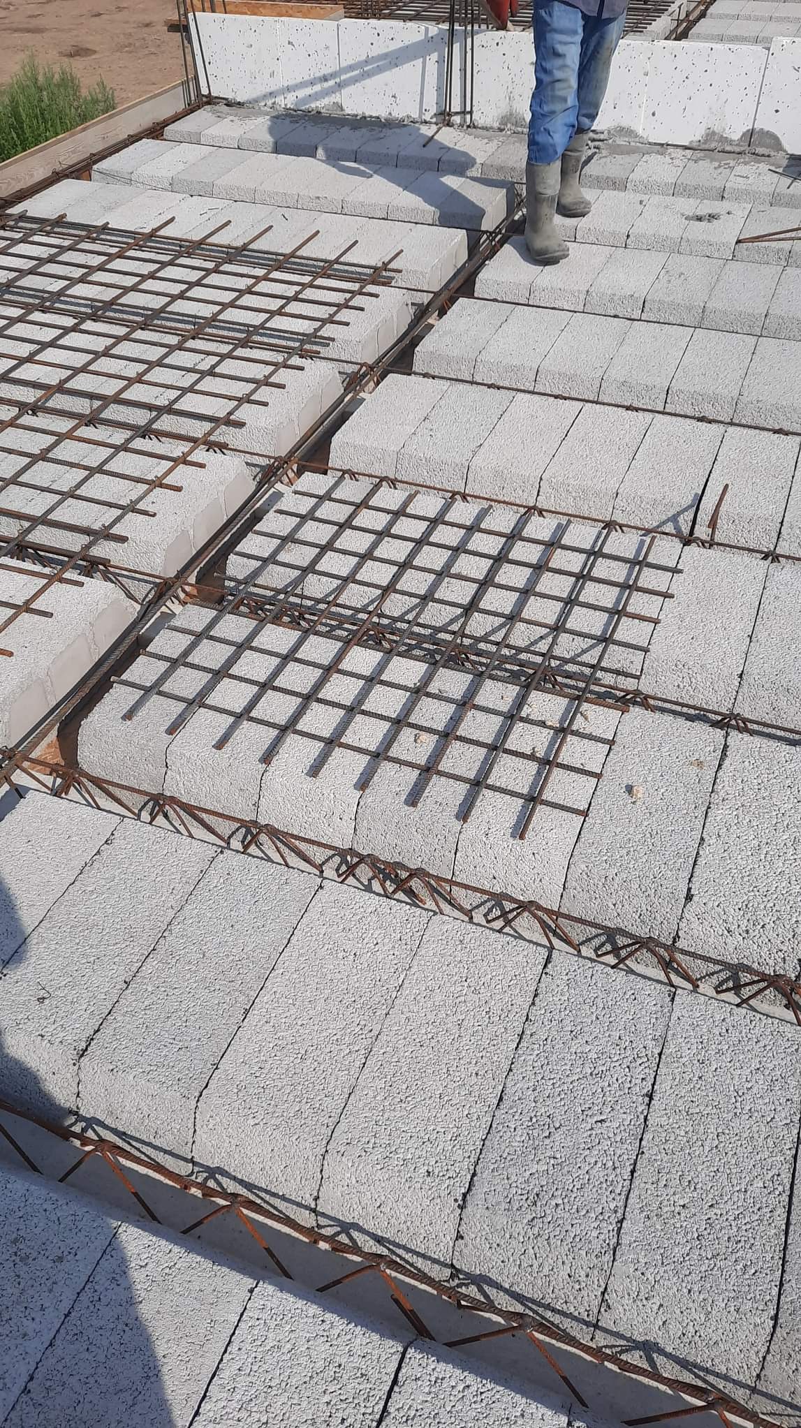 Wiązanie zbrojenia na stropie z szarego bloczka betonowego, widoczne fragmenty szalunku.