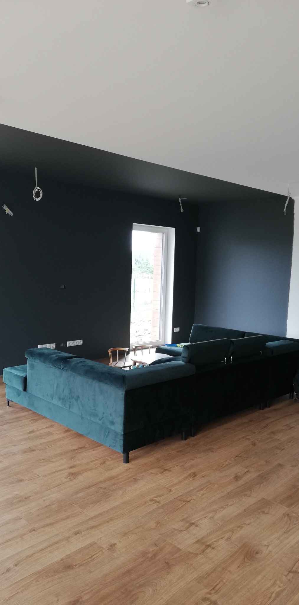 Pomieszczenie po remoncie z ciemnymi ścianami i sufitem, z widocznymi przewodami elektrycznymi przed montażem oświetlenia, oraz turkusowym narożnikiem na drewnianej podłodze.