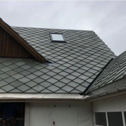 Krystian Wójs DACHYWOJS - Szary dach z dachówką rombową i oknem dachowym. Fragment drewnianej ściany budynku z oknami. Montaż orynnowania.