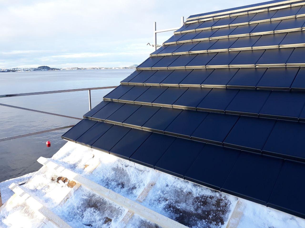 Czarne dachówki ceramiczne ułożone na połaci dachu z widokiem na morze. Śnieg na więźbie. Nowoczesny design pokrycia dachowego.