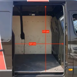 Wnętrze pustego, wyłożonego sklejką busa z otwartymi drzwiami bocznymi, z naniesionymi wymiarami 177 cm wysokości i 127 cm szerokości.