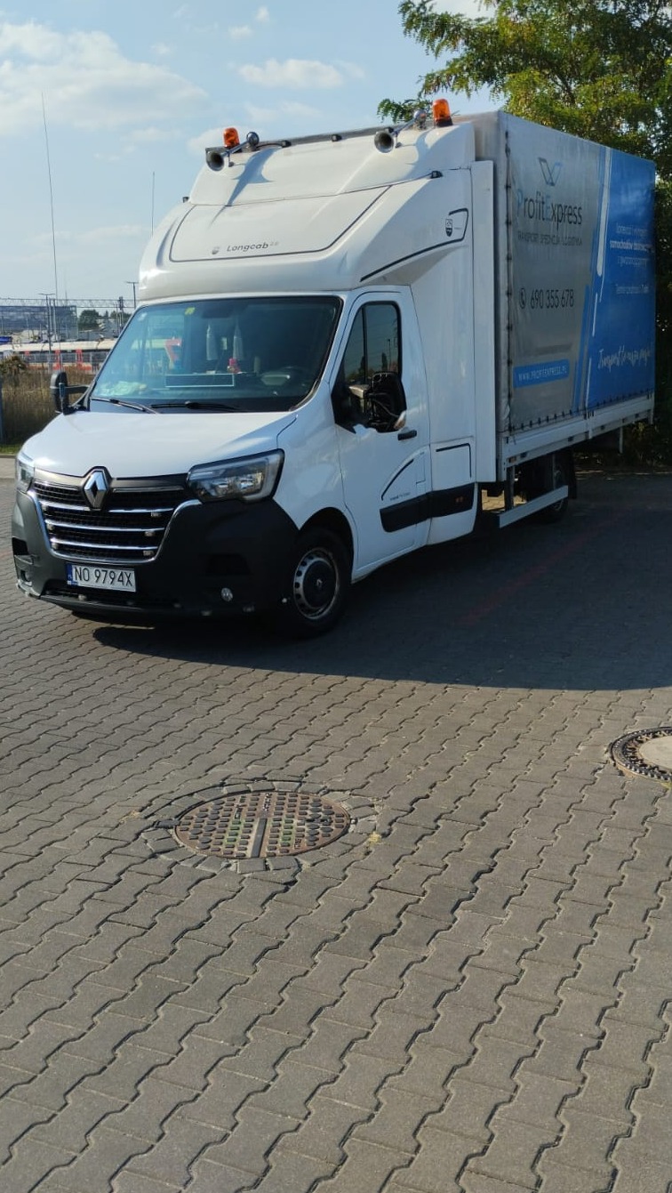 Biały samochód dostawczy Renault Master z zabudową plandekową i logo firmy transportowej Profit Express, zaparkowany na brukowanym placu w słoneczny dzień.