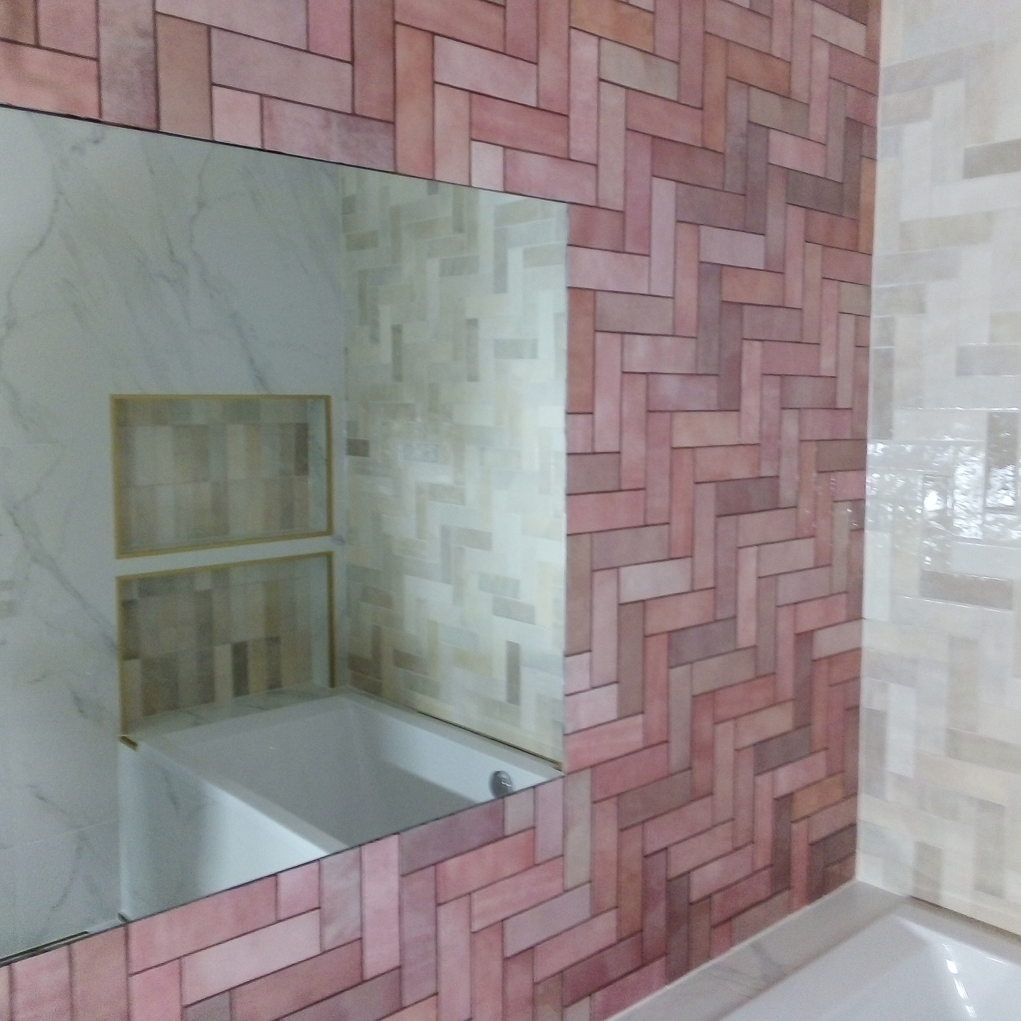 Ukończona łazienka z różową cegiełką ułożoną w jodełkę i lustrem odbijającym wannę oraz wnęki wykończone płytkami.