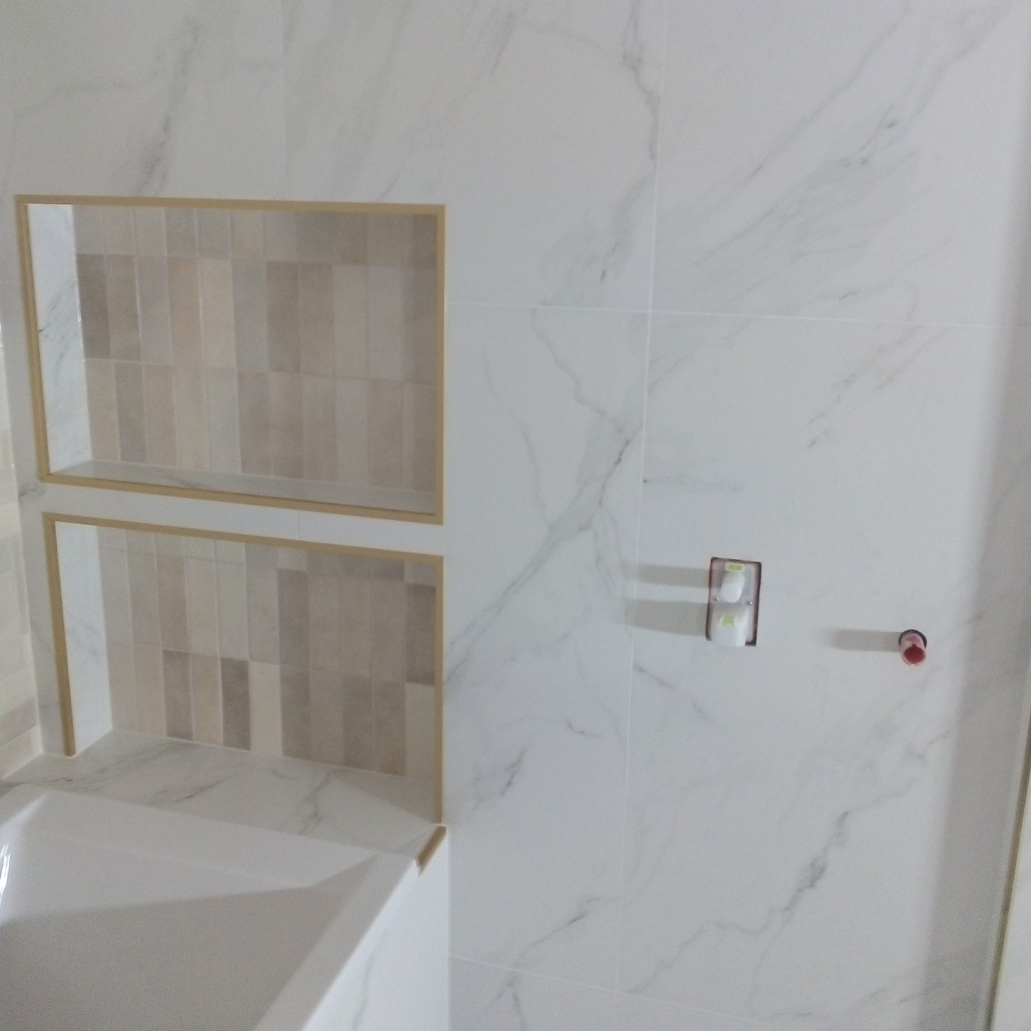 Wykończona łazienka z białymi marmurkowymi płytkami, wnęki z mozaiką w odcieniach beżu i brązu, widoczna wanna.