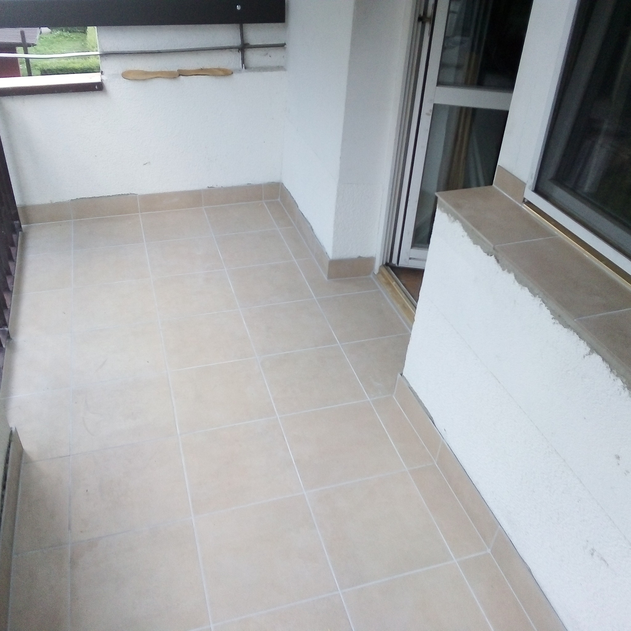 Wykończony balkon z beżowymi płytkami w Lublinie, widoczne fragmenty okna i balustrady.