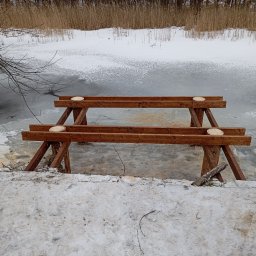 Mirosław Gielka - Brązowa, drewniana konstrukcja w trakcie budowy na tle zamarzniętego jeziora i lasu; widoczne ślady cięcia drewna i śnieg.