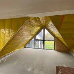 Nikon Construction Heorhii Nikonenko - Poddasze z oknem trójkątnym, ocieplone żółtą folią z czerwonymi paskami, widoczne płyty izolacyjne. Etap prac przed wykończeniem.