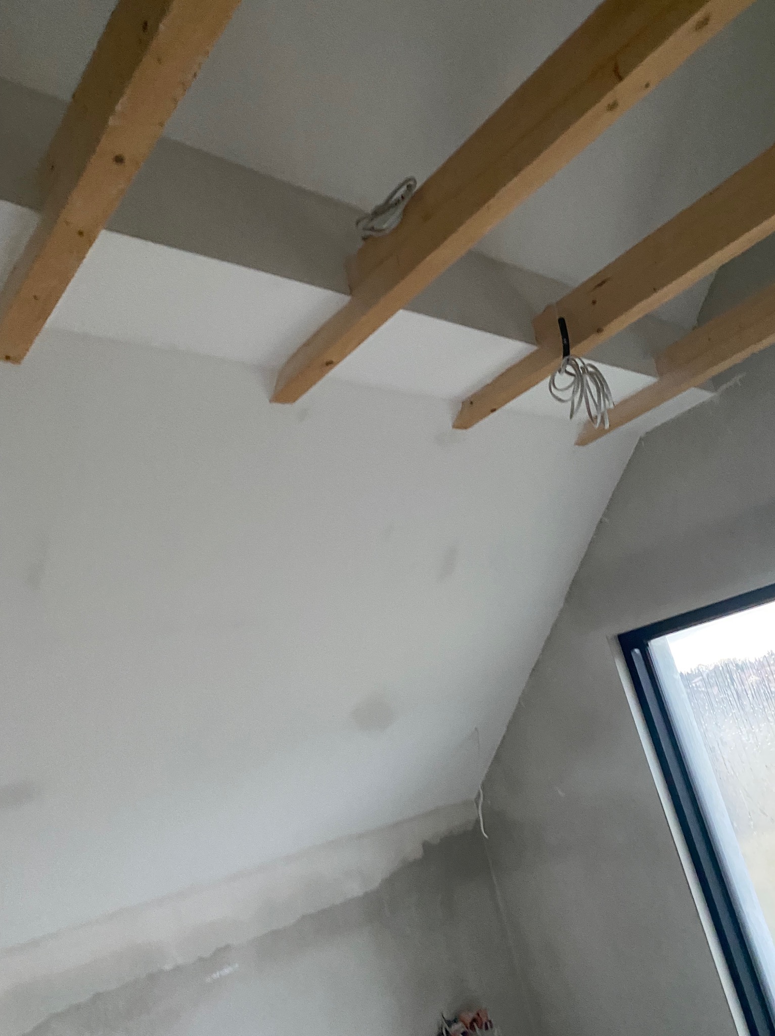 Skośny sufit poddasza z drewnianą konstrukcją i częściowo położoną płytą gipsową, widok z dołu, Kraków. Widoczne kable elektryczne.