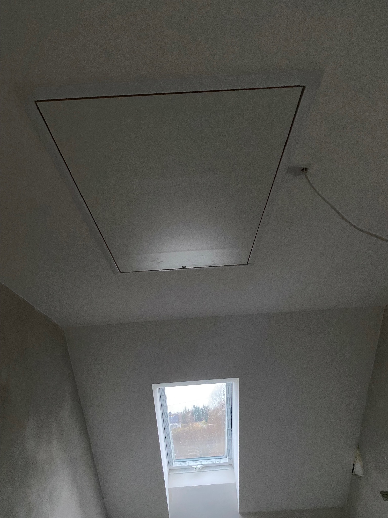 Wykończone poddasze z oknem dachowym i klapą rewizyjną w suficie. Ściany przygotowane do malowania, widoczne gładzie. Minimalistyczny design.